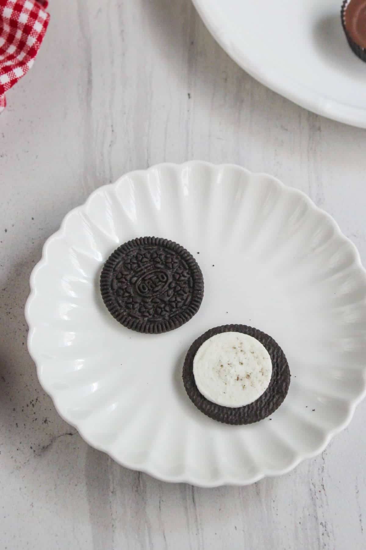 A white plate holds two chocolate sandwich cookies, one whole and one separated to show the cream filling.