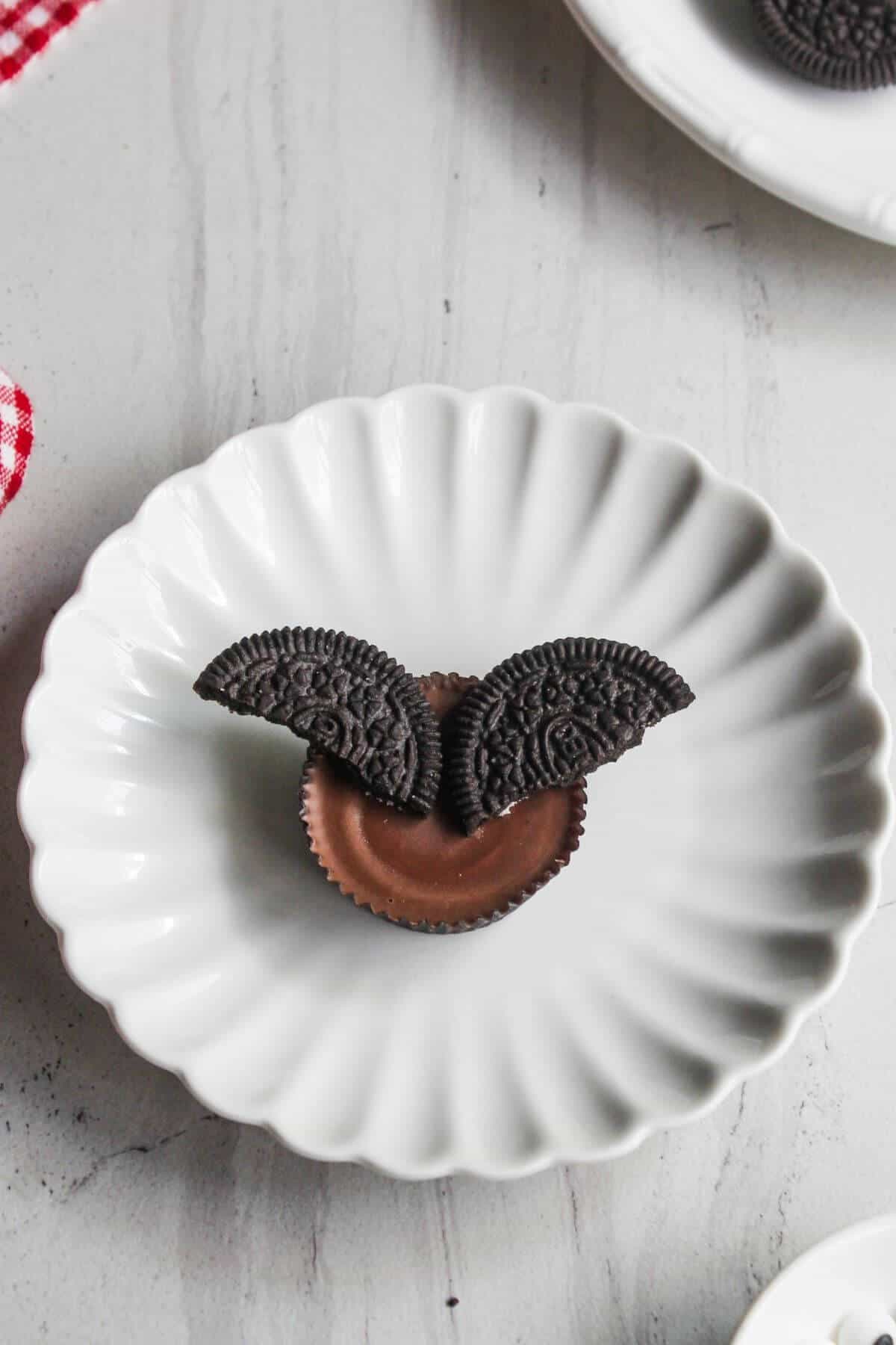 A chocolate cup topped with two Oreo cookie halves is placed on a white scalloped plate.