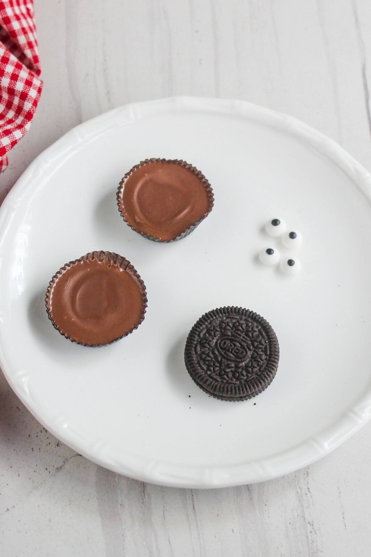 A white plate with two peanut butter cups, one chocolate sandwich cookie, and three small candy eyes on it.