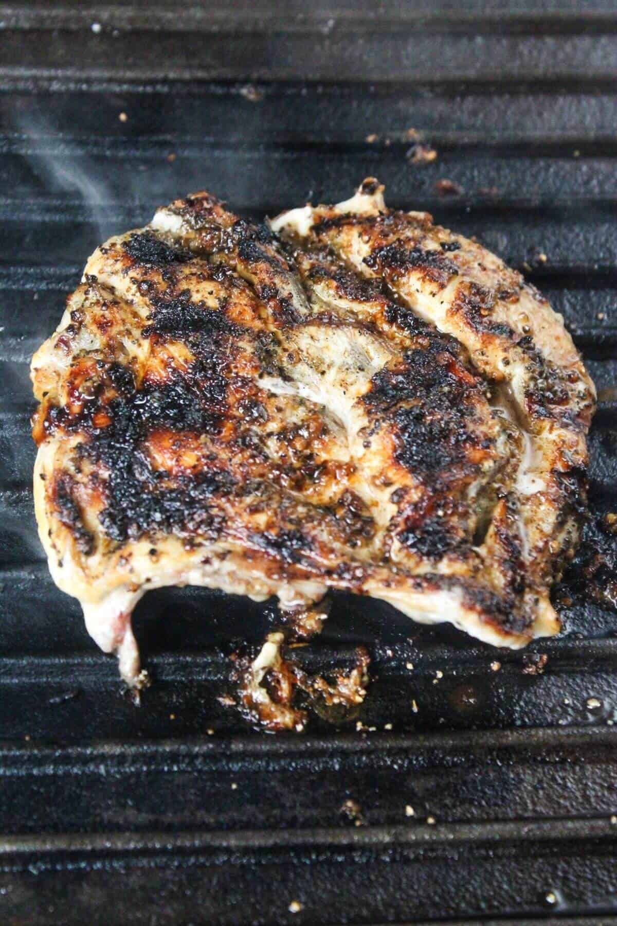 A piece of seasoned meat with char marks is cooking on a grill, showing seared and blackened areas.