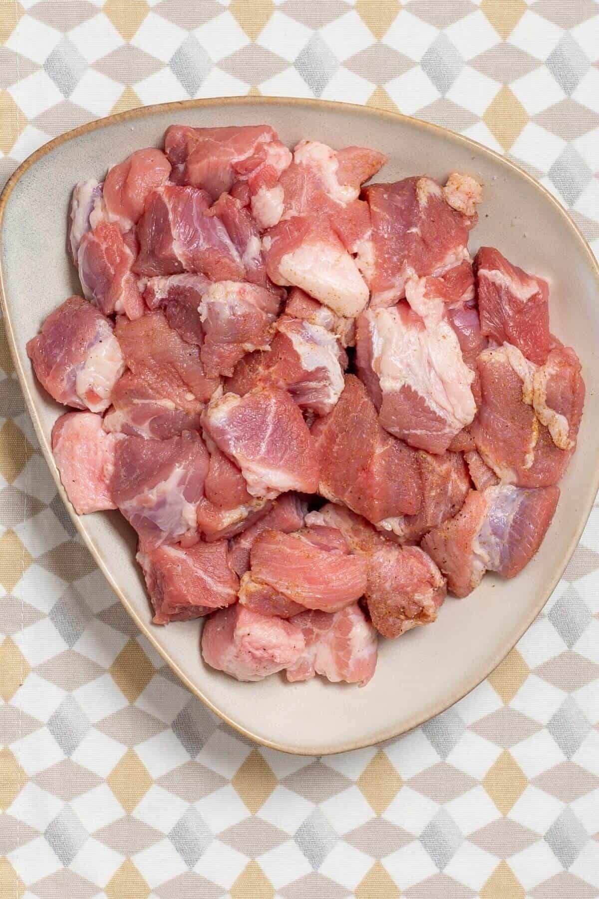 Raw, cubed pork pieces seasoned with spices in a shallow bowl.