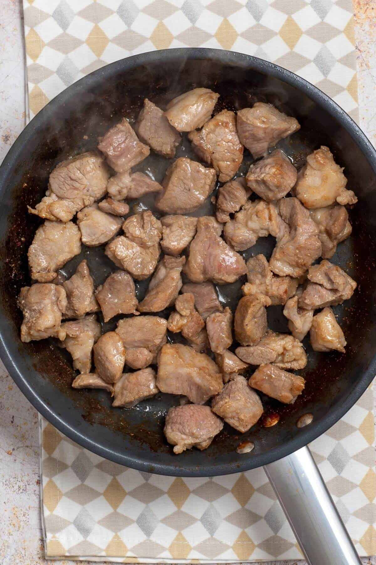 Bite-sized pieces of pork searing in a frying pan.