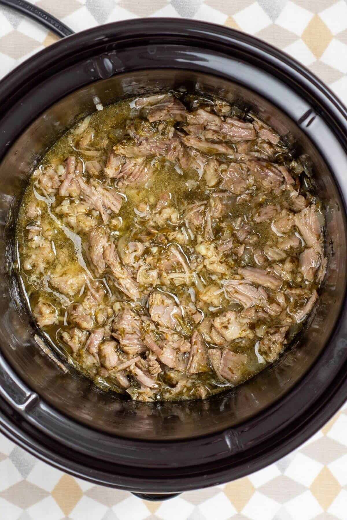 Shredded meat in a savory broth inside a slow cooker.