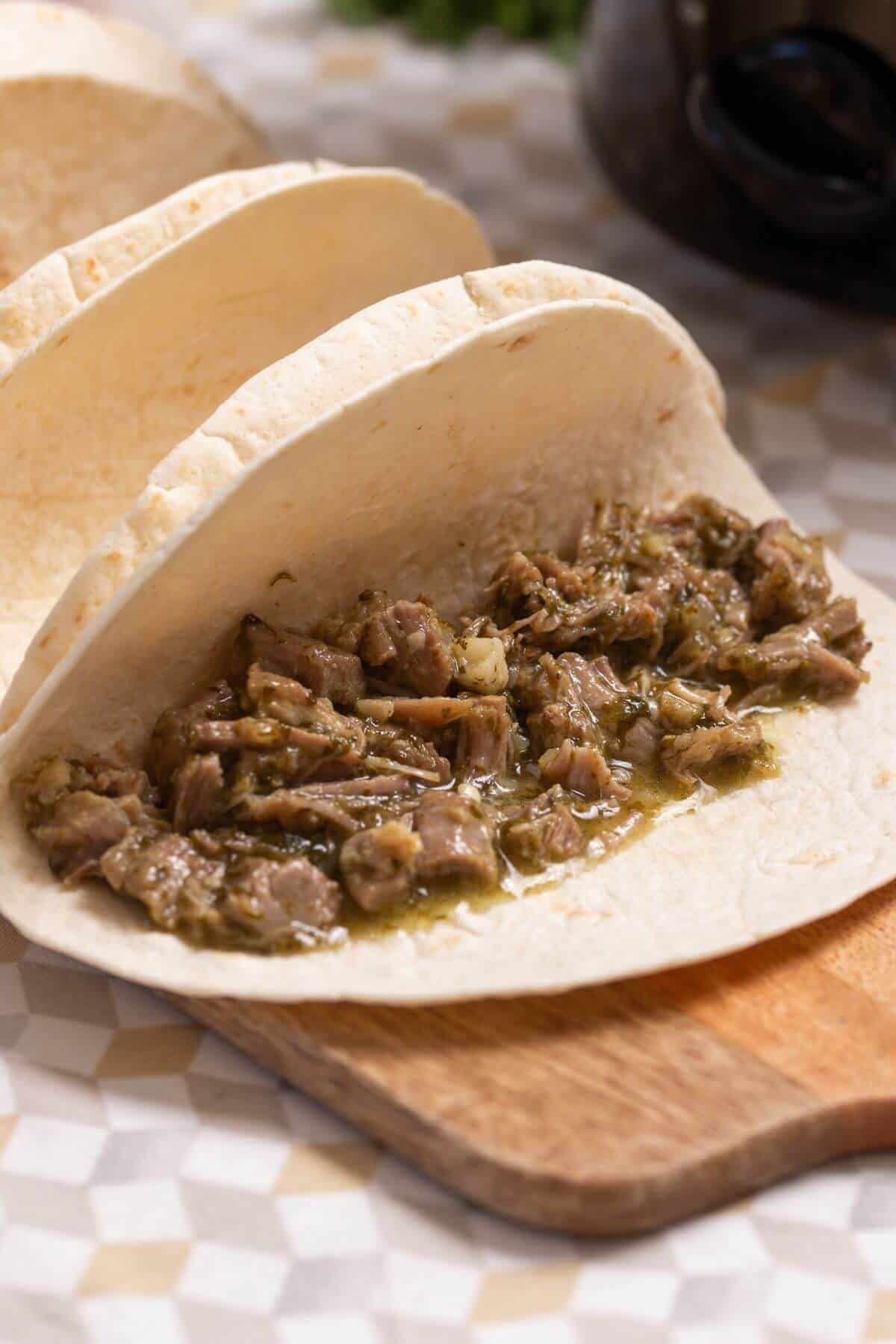 A flour tortilla taco filled with shredded pork in green salsa.