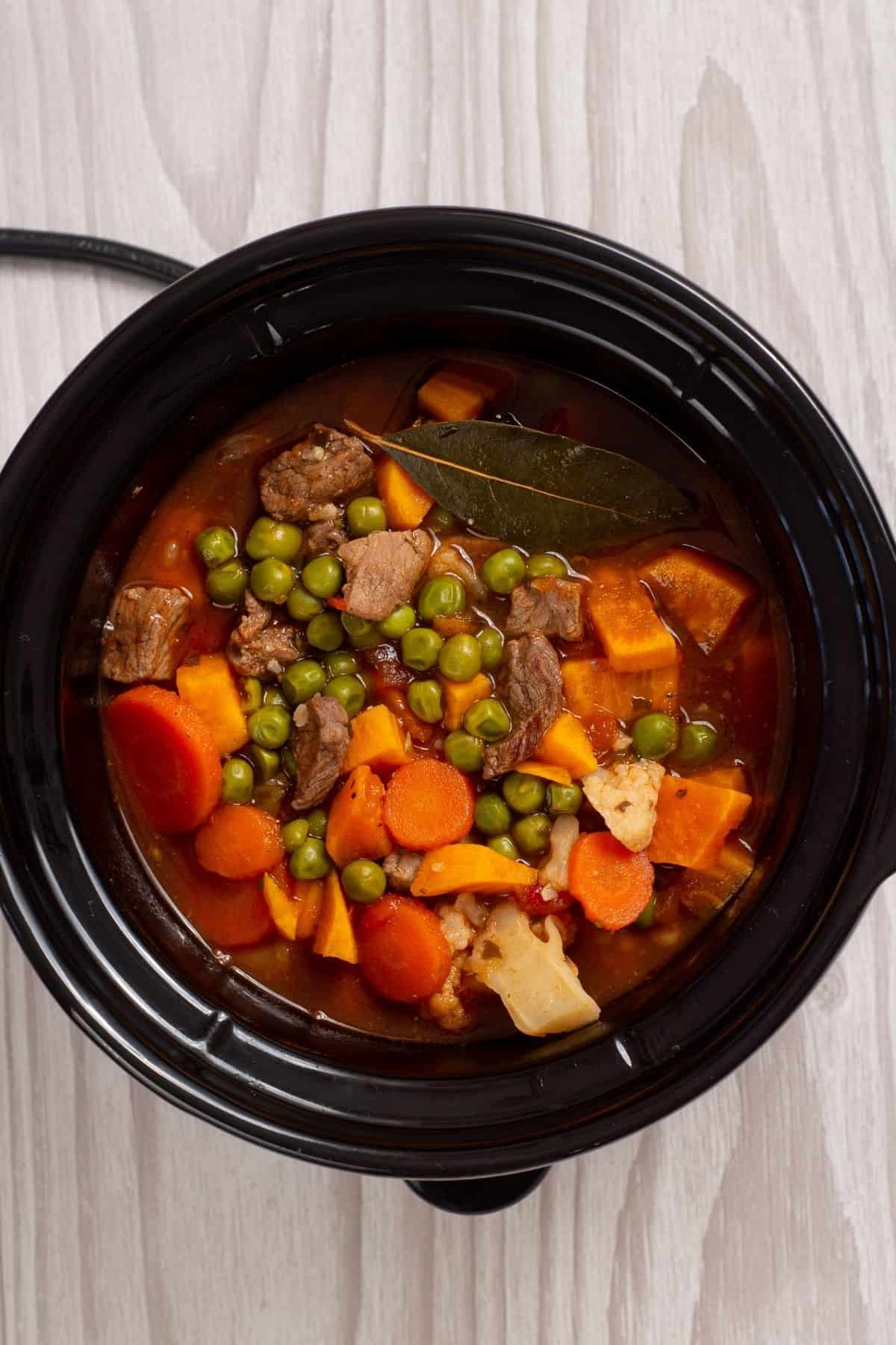 Beef stew with carrots, peas, and cauliflower in a slow cooker pot.
