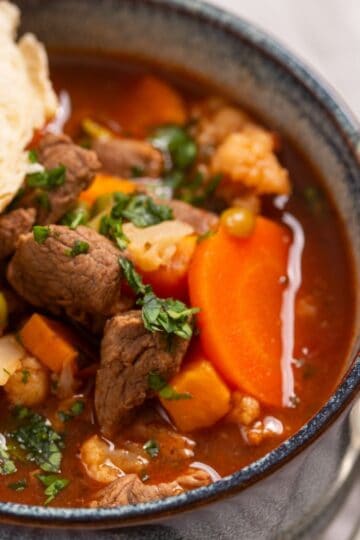 A bowl of beef stew with carrots, peas, and cauliflower, served with a piece of bread.