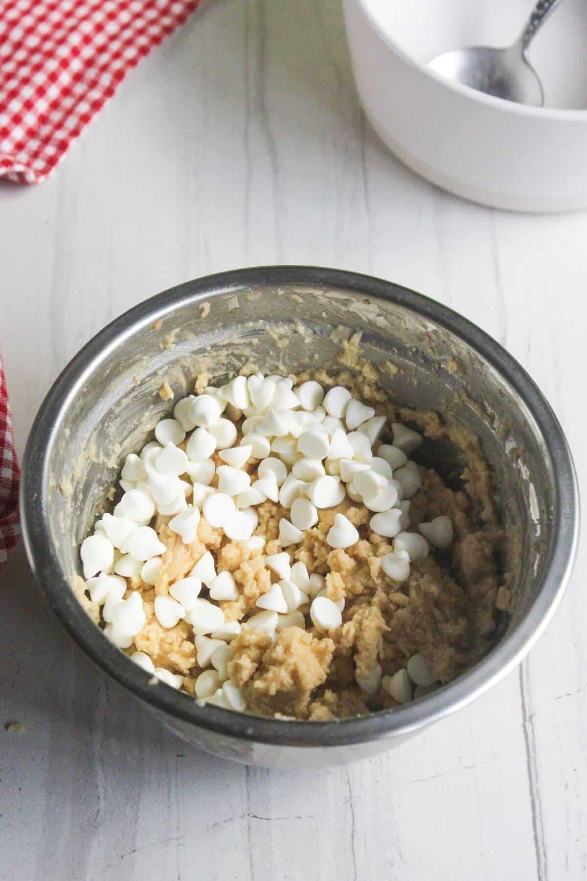 A stainless steel bowl filled with cookie dough topped with white chocolate chips.