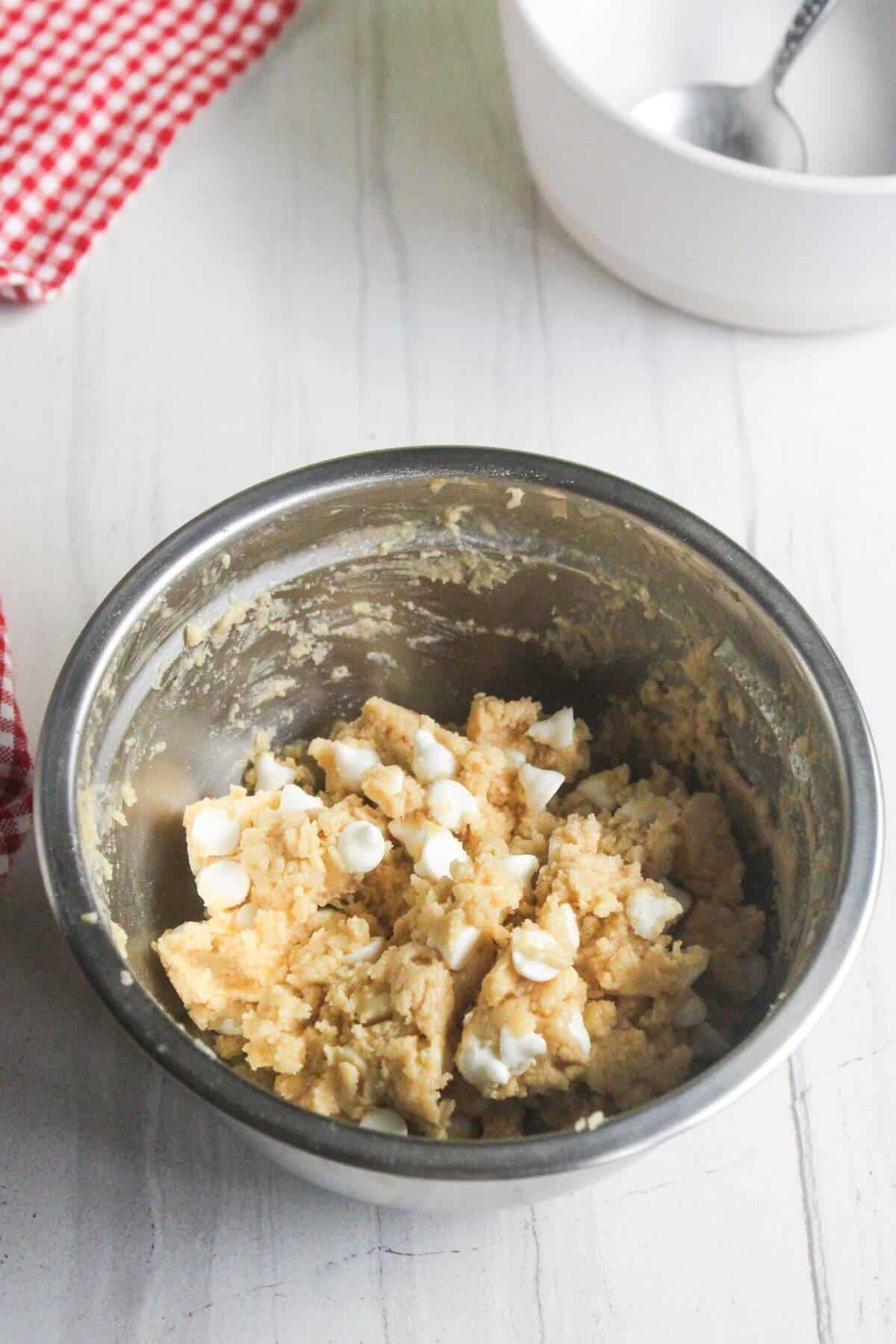 Cookie dough mixed with white chocolate chips in a metal mixing bowl.