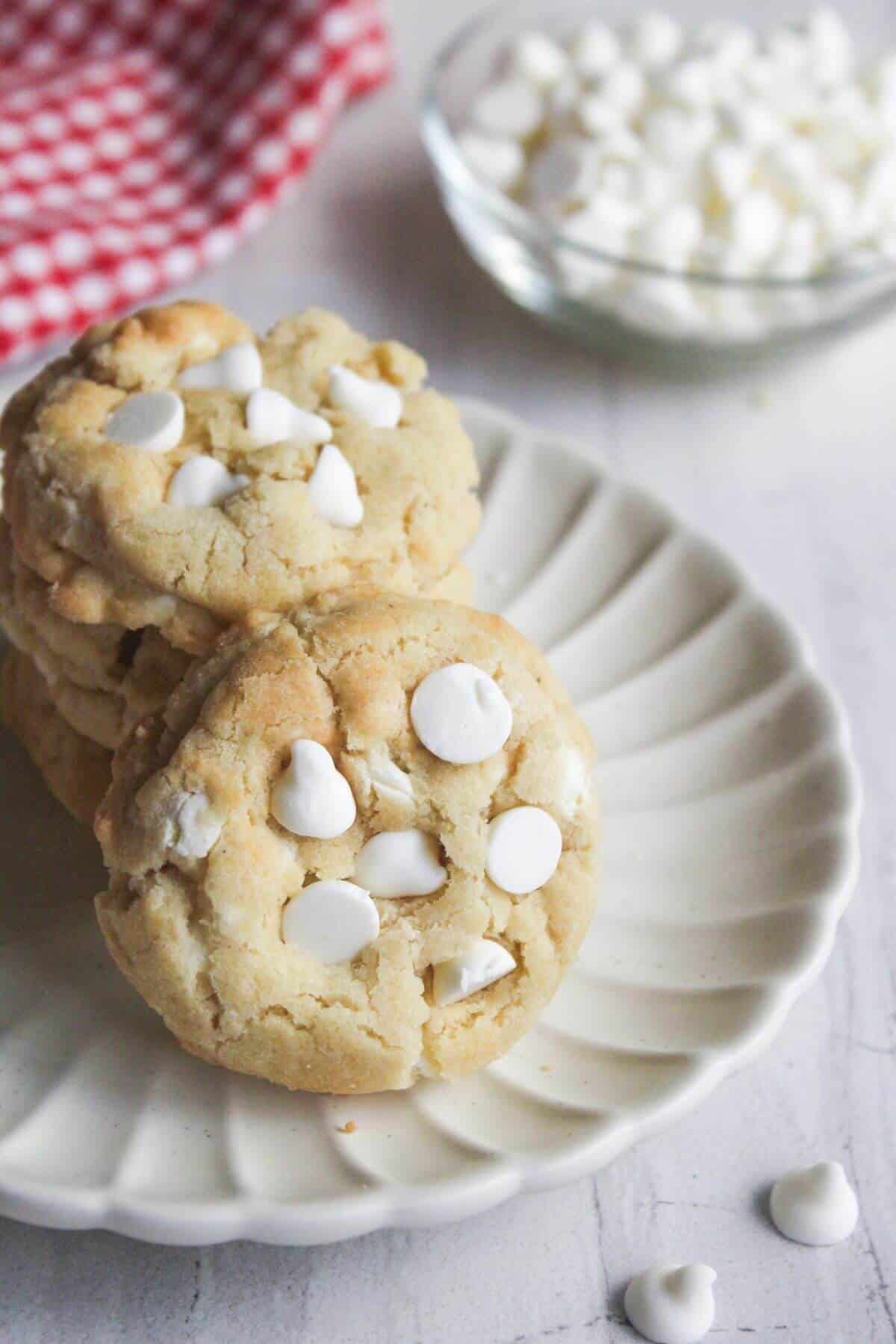 A stack of white chocolate chip cookies on a scalloped plate.